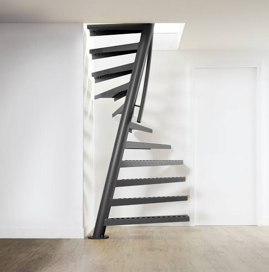 Ultra-compact space-saving spiral staircase with a single central charcoal pole and cantilevered alternating metal treads set against a white wall