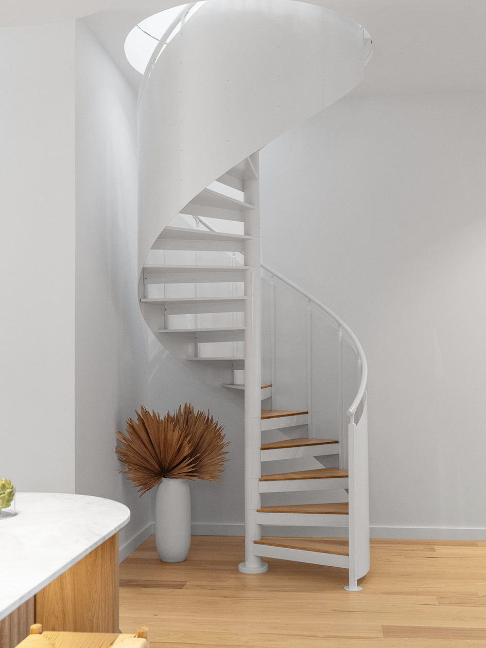 Satin-white spiral staircase with warm timber treads and solid white screens leading up to an attic in a bright Sydney home